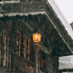 Wooden cottage with burning lantern during snowfall
