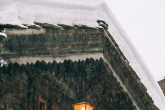 Wooden cottage with burning lantern during snowfall