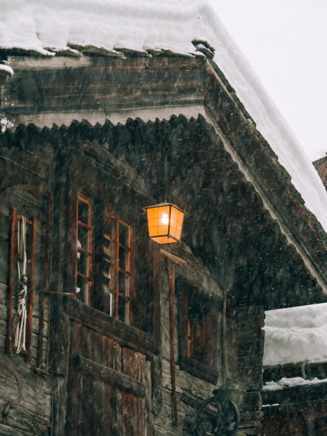 Wooden cottage with burning lantern during snowfall