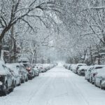 snow covered road with cars parked on side